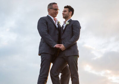 Photo of two grooms holding each other with the sun setting behind them.