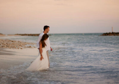 Photo of a bride and groom walking in to the ocean at Fort Zach beach.