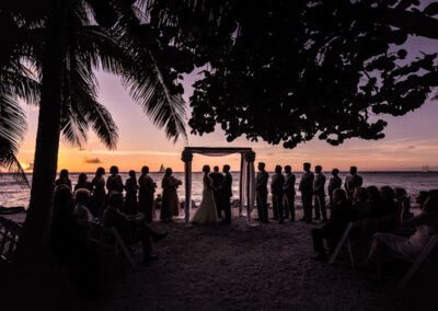 Silhouette photo of a bridal party with the bride and groom in the middle saying their vows during sunset.